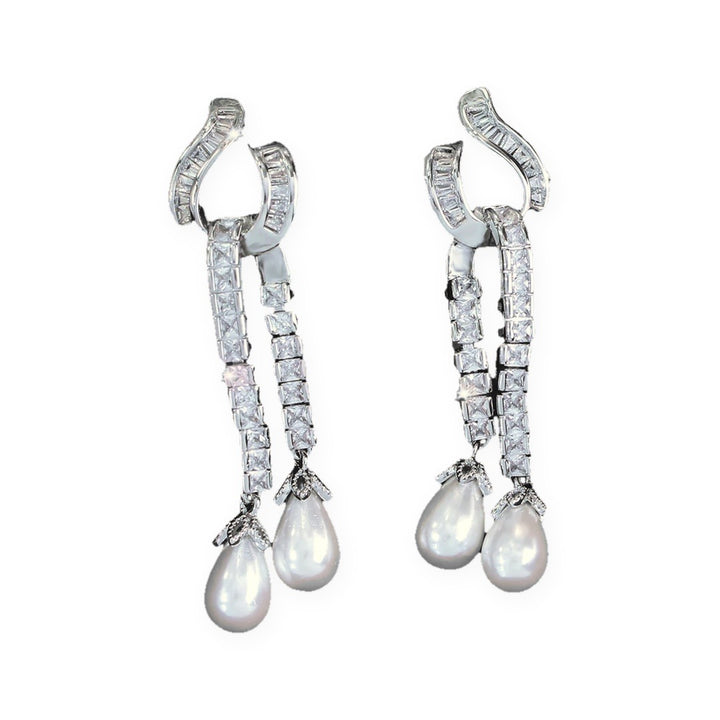 Pair of silver-tone Seraphina drop earrings with baguette cubic zirconia hooks, double square-zirconia strands and faux pearl teardrops, on a white background